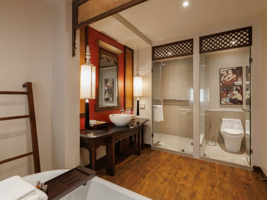 A modern bathroom with a wooden floor, a large mirror, a sink, a toilet, and a glass-enclosed shower.
