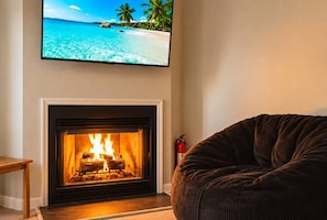Un salon avec une cheminée, un téléviseur diffusant une scène de plage et un fauteuil en forme de sac de haricots.