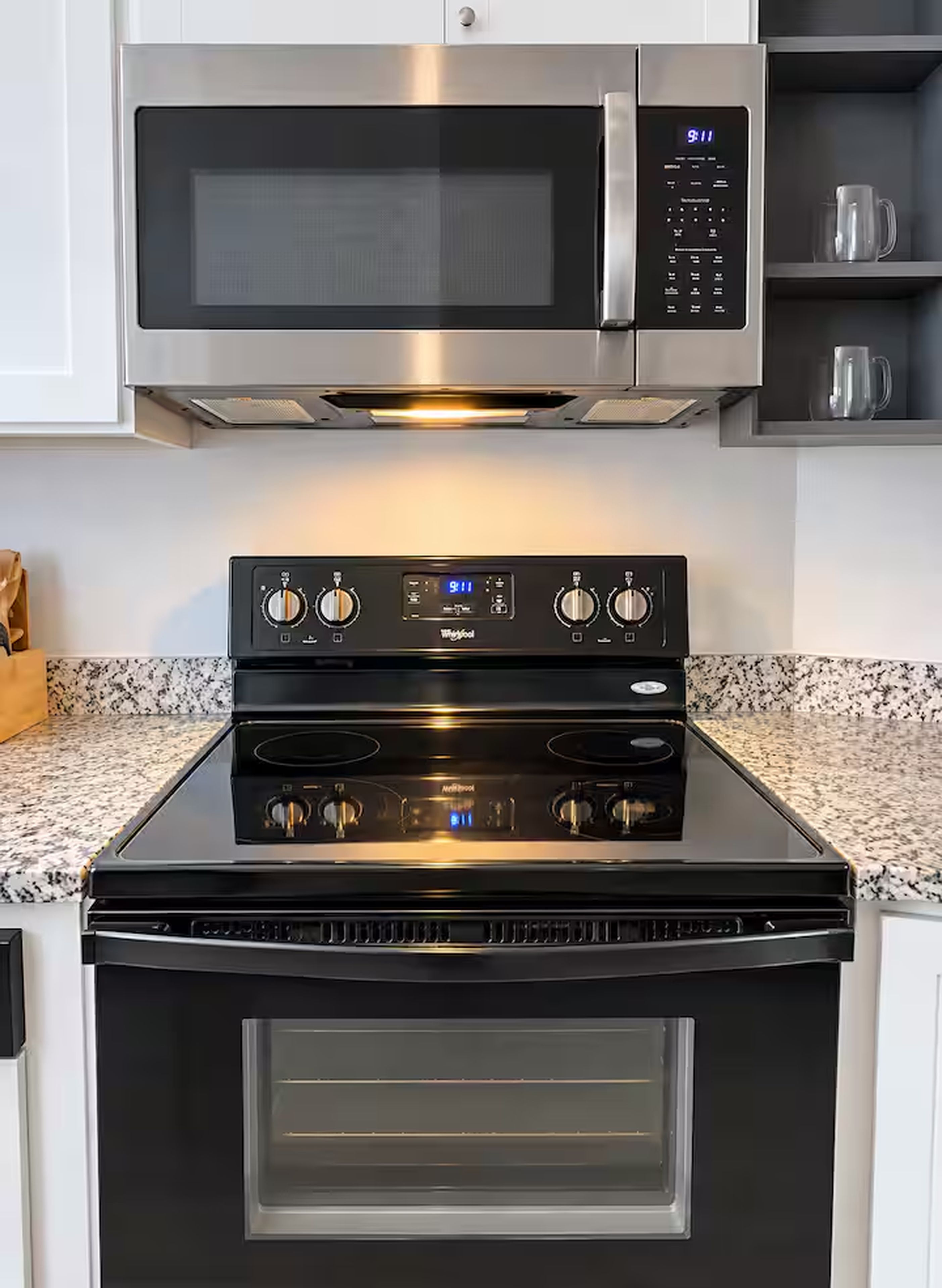 A kitchen with a stainless steel microwave above a black stove with a digital clock.