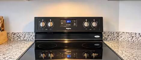 A kitchen with a stainless steel microwave above a black stove with a digital clock.
