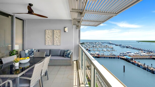 A balcony with a dining area, a ceiling fan, and a view of a marina with boats. - Belle Escapes 52 Harbour Lights with Ocean View (Cairns City)