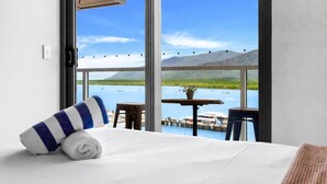 A hotel room with a large window offering a view of a lake and boats, a bed with a striped pillow, and a small table with a plant. - Belle Escapes 52 Harbour Lights with Ocean View (Cairns City)
