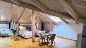 A spacious loft bedroom with a large bed, a dining area with a table and chairs, and a kitchen area with a refrigerator.