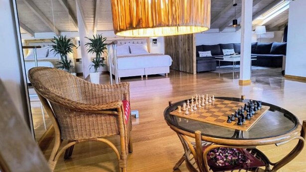 A spacious living area with a round glass table for chess, wicker chairs, and a hanging light fixture.