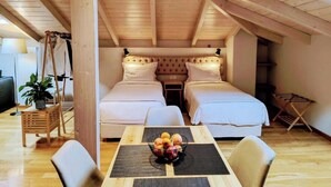 A cozy attic bedroom with two beds, a dining table with fruit, and wooden beams on the ceiling.