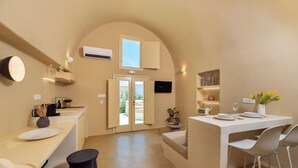 Et moderne køkken med hvælvet loft, et spiseområde med bord dækket til to og et lille siddeområde med en skammel.