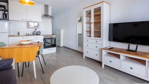 A modern kitchen with white cabinets, a dining area with a wooden table and chairs, and a TV on a wooden stand. - Tenerife Royal Gardens - Beachfront Bliss. Studio Apartment Sea/Pool views. (Playa de la Américas)