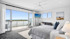 Een slaapkamer met een groot bed, een balkon met uitzicht, een plafondventilator en een televisie.