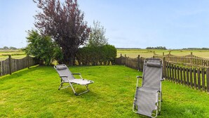 Deux chaises de jardin sont placées dans un espace herbeux, avec une clôture en bois et un arbre en arrière-plan.