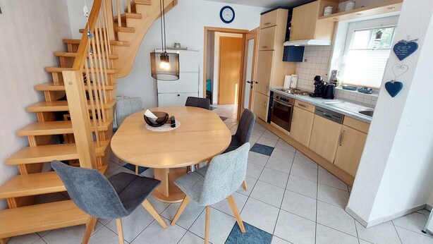 Cocina compacta con una escalera de madera, una mesa redonda con sillas y un ventanal pequeño.