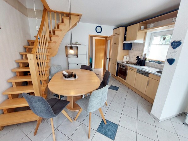 A compact kitchen with a wooden staircase, a round dining table with chairs, and a small window. - Ferienunterkunft in Dornumergrode (Dornum)