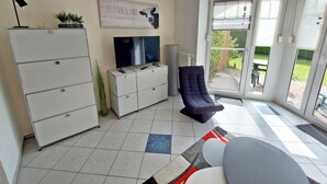 Una sala de estar con televisor, sofá, sillón, aparador y puerta corrediza de vidrio que da a un espacio exterior.