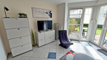 A living room with a TV, a sofa, a chair, a cabinet, and a sliding glass door leading to an outdoor area.