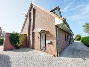 A brick building with a sloped roof, a door with a mailbox, and a paved driveway. - Ferienunterkunft in Dornumergrode (Dornum)