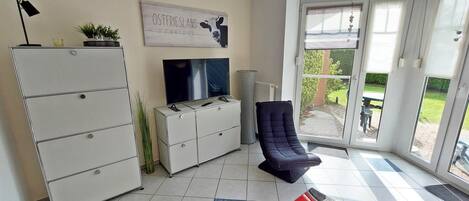 Een woonkamer met een televisie, een bank, een stoel, een kast en een schuifdeur die uitkomt op een terras.