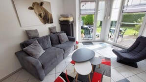 Un salon moderne avec un canapé gris, un fauteuil noir, une petite table ronde et un tapis coloré.