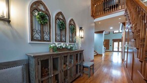 A spacious hallway with wooden flooring, a built-in cabinet with glass doors, and a staircase with wooden railings.