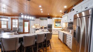 A modern kitchen with wooden ceiling, stainless steel appliances, and a central island with bar stools.