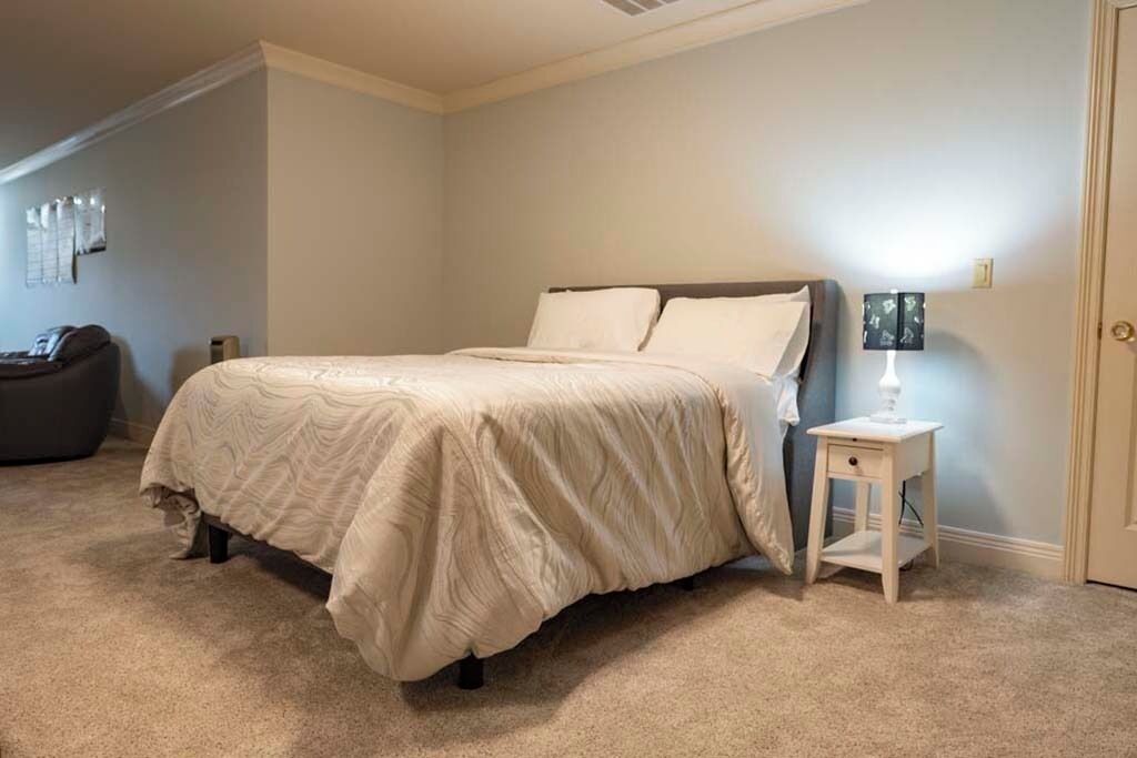 A bedroom with a bed, a nightstand, a lamp, and a chair.