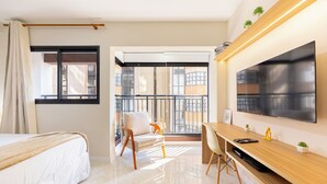A modern hotel room with a bed, a desk, a chair, a TV, and a balcony with a view of buildings. - OCB - Luxo e Conforto Campo Belo (São Paulo)