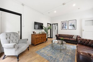 A living room with a grey armchair, a brown leather sofa, a wooden cabinet, a television, and framed pictures on the wall. - 23A Bevenden Street (Greater London)