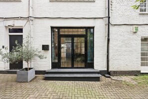 A building with a white brick exterior, a black door with glass panels, and a small step leading to the entrance. - 23A Bevenden Street (Greater London)