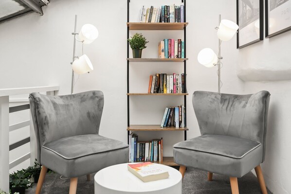 Two grey armchairs facing each other with a bookshelf and a small table between them.