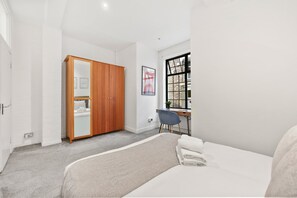 A bedroom with a bed, a desk, a chair, a wardrobe, and a window. - 23A Bevenden Street (Greater London)
