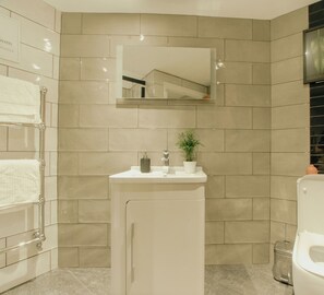 Ein modernes Badezimmer mit einem weißen Waschbecken, einem Spiegel und einer Pflanze.