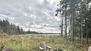 Een camping met twee houten stoelen en een vuurkuil, omringd door bomen en een grasveld.