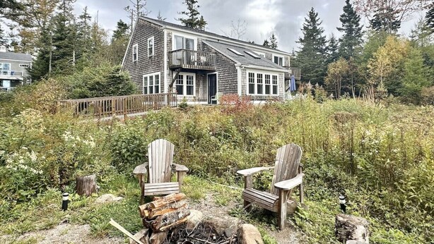 Een huis met een terras, omringd door weelderige begroeiing en een vuurplaats met twee Adirondack stoelen.