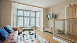 A living room with a leather sofa, a glass coffee table, a TV mounted on the wall, and a window with curtains. - Stunning Quiet Apartment in Historic Building (Sheffield)