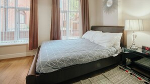 A bedroom with a bed, a bedside table with a lamp, a clock, and a window with curtains. - Stunning Quiet Apartment in Historic Building (Sheffield)