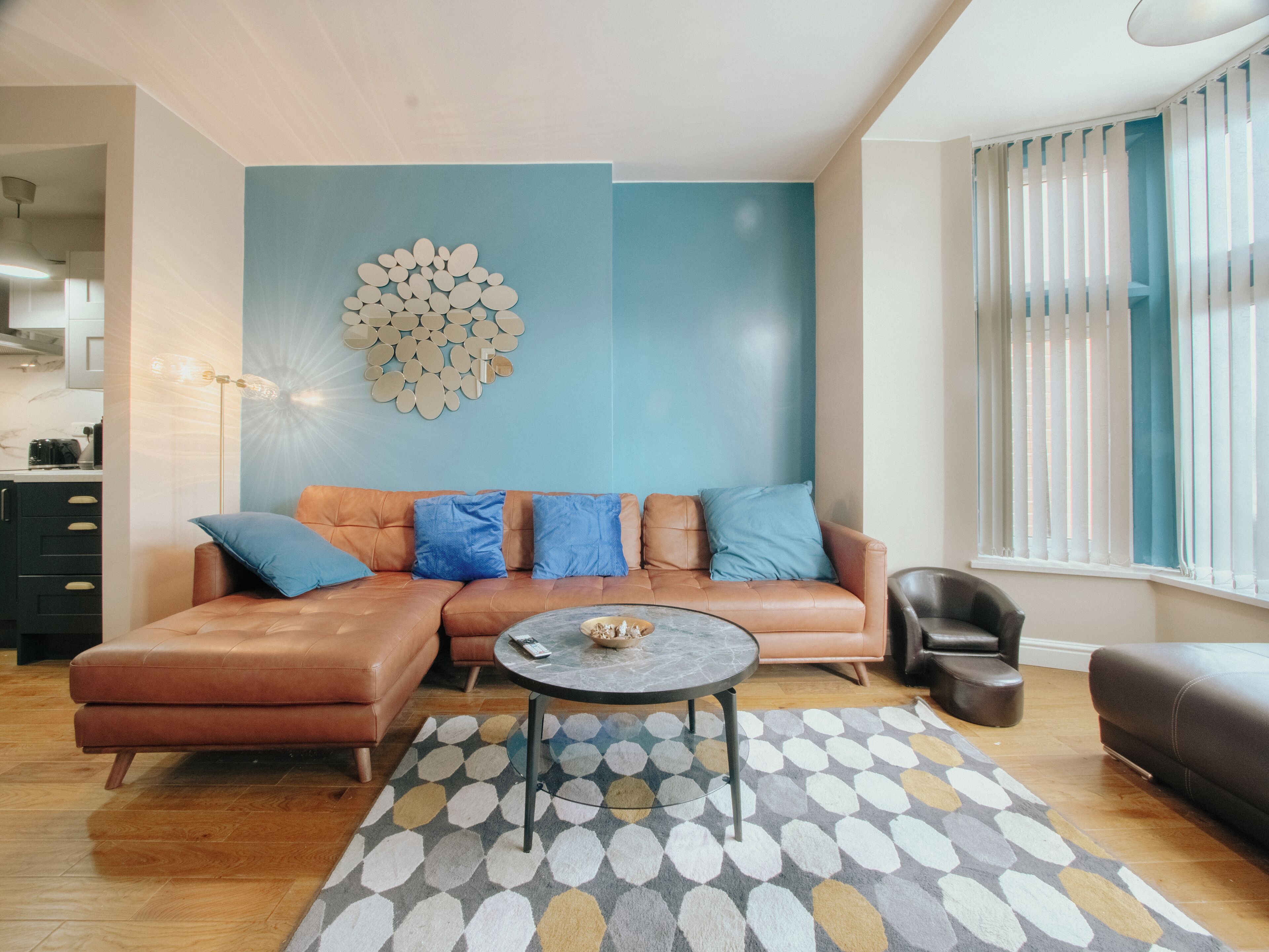 Ein modernes Wohnzimmer mit einem braunen Ledersofa, blauen Kissen, einem runden Couchtisch und einem Teppich mit geometrischem Muster.