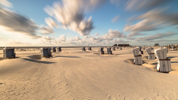 A beach with rows of white beach chairs and a sandy landscape. - Ferienwohnung in St. Peter-ording (St. Peter-Ording)
