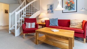 A living room with a red sofa, a wooden coffee table, a red armchair, a white staircase, and a painting on the wall. - Ferienwohnung in St. Peter-ording (St. Peter-Ording)