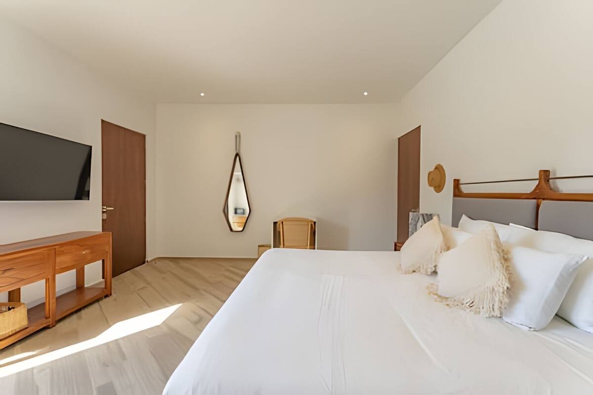 A modern hotel room with a large bed, a wooden desk, a television, and a mirror on the wall.