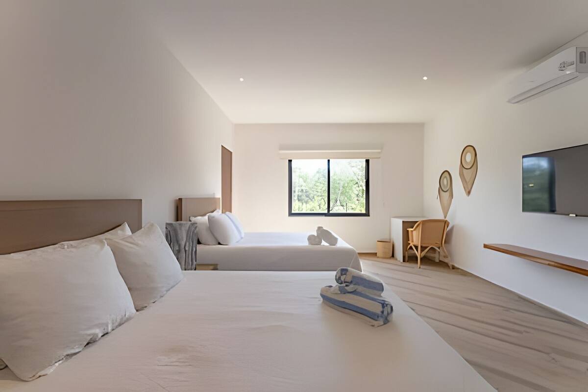 A modern hotel room with two beds, a desk, a chair, and a TV.