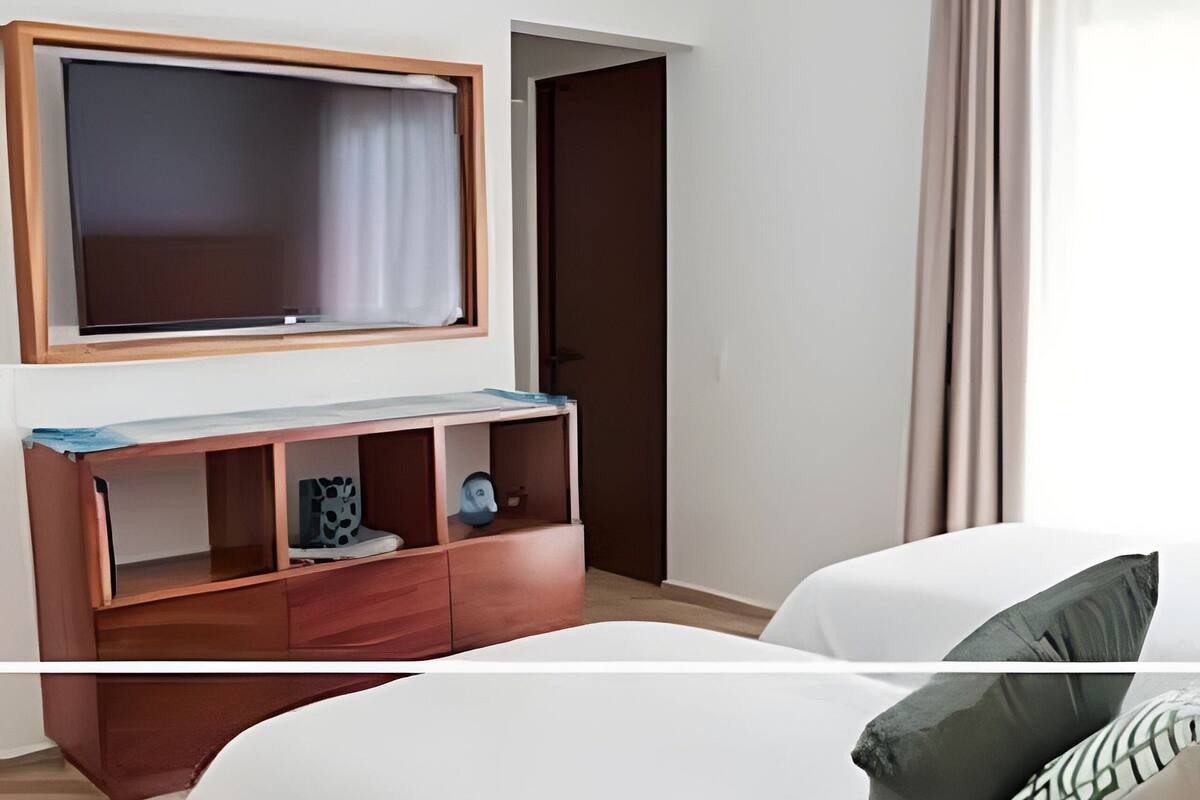 A hotel room with a bed, a TV mounted on the wall, a wooden cabinet, and a door.