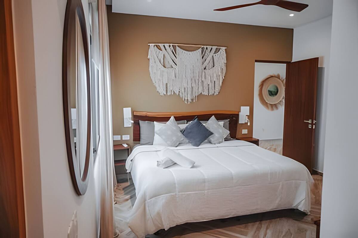 A bedroom with a bed, a wooden headboard, a wall-mounted macrame piece, and a door with a circular design.
