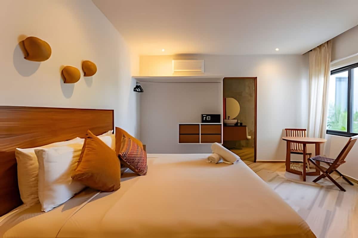 A modern hotel room with a large bed, a wooden headboard, a desk with a chair, and a view of the outdoors.