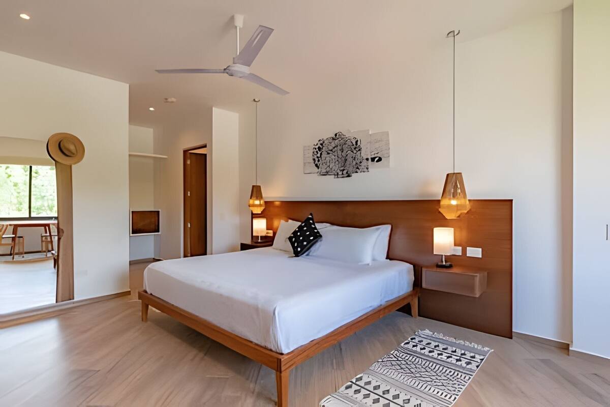 A modern bedroom with a wooden bed, two bedside lamps, a ceiling fan, and a large window.