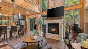 A spacious living area with a fireplace, wooden floors, and a high ceiling. - INDOOR HEATED POOL CABIN SLEEPS 10 & GAME LOFT “BEAR SPLASH” NEAR PARKWAY! (Sevierville)