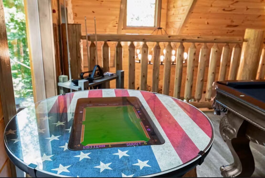 Een pooltafel met een Amerikaans vlagdesign, een poolkeu-rek en een biljarttafel in een houten ruimte met een houten hek en een raam.