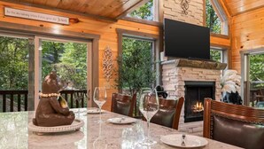 A dining area with a marble table, chairs, a fireplace, and a television mounted on the wall. - INDOOR HEATED POOL CABIN SLEEPS 10 & GAME LOFT “BEAR SPLASH” NEAR PARKWAY! (Sevierville)