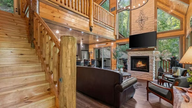 A spacious wooden interior with a fireplace, a staircase, and a dining area. - INDOOR HEATED POOL CABIN SLEEPS 10 & GAME LOFT “BEAR SPLASH” NEAR PARKWAY! (Sevierville)