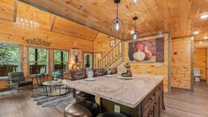 A wooden cabin interior with a dining area, kitchen, and a staircase leading to a loft. - INDOOR HEATED POOL CABIN SLEEPS 10 & GAME LOFT “BEAR SPLASH” NEAR PARKWAY! (Sevierville)