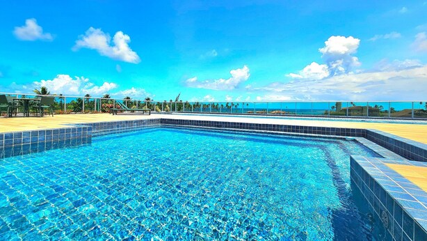 Une piscine d’un bleu éclatant, bordée de carreaux, entourée d’une terrasse avec des chaises et offrant une vue sur l’océan.