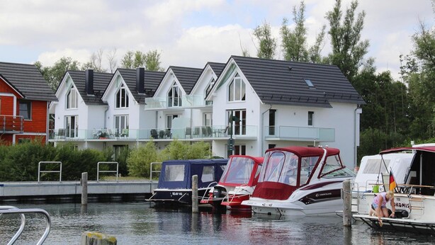 A row of modern houses with balconies, a dock with boats, and a calm water body. - Reihenhaus Hafenflair am Plauer See (Plau am See)