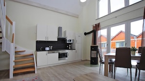 A compact kitchen with white cabinets, a microwave, and a stove. There is a dining area with a table and chairs, and a staircase leading to another level. - Reihenhaus Hafenflair am Plauer See (Plau am See)